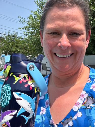 Reviewer smiling outdoors, holding the colorful shark-print Bottle Buddy 24oz water bottle.
