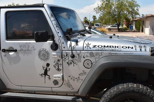 Customer's silver Jeep covered in custom black vinyl decals with petroglyph-style designs, including the word 'ZOMBICON' on the hood.