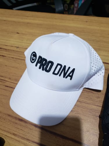 Customer's white PRO DNA Weatherproof Snapback Hat with black puff embroidery, sitting on a wooden table.