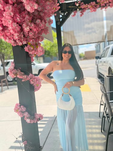 Customer smiling in the strapless Bianca Tube Midi Dress on an outdoor patio under pink flowers.