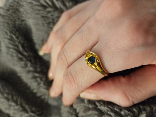 Customer's hand wearing the yellow-gold Celestial Blue Star Ring with a dark blue stone on a fluffy grey surface.