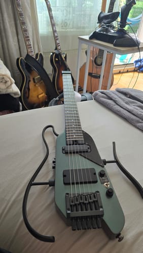 Ein Rezensent zeigt seine grüne Donner HUSH X PRO E-Gitarre, die auf einem Bett liegt.