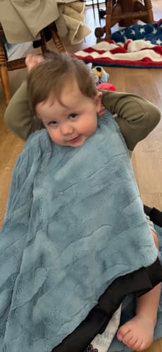 Customer's child wrapped in the blue plush back of the Choo Choo Blanket, which has a black satin ruffle.