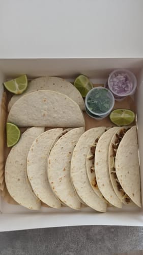 Klant toont een doos met gemaakte Birria-taco's, tortilla's en verse toppings zoals limoen.