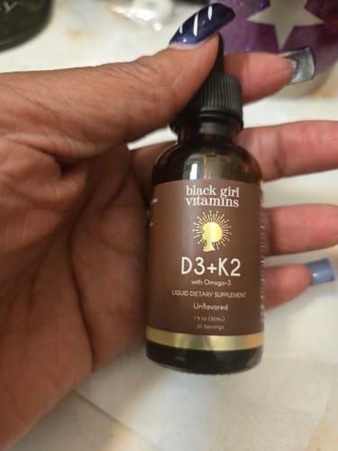 A reviewer's hand holding the brown dropper bottle of Vitamin D3 + K2 Drops.