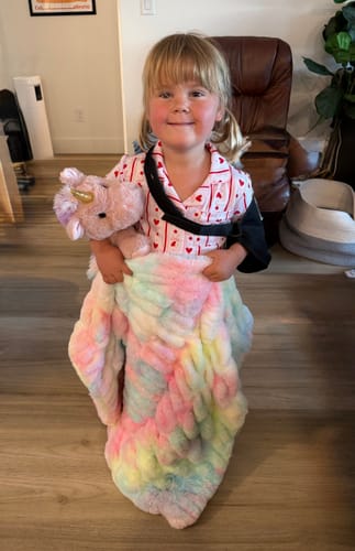 Reviewer's smiling child holds the plush Hugs Tie Dye Pastel Blanket while wearing an arm sling.