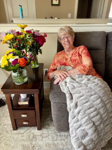 Reviewer's photo of a person smiling on a recliner with the soft gray Hugs Tranquil Dove Blanket.