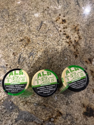 Customer's three cans of ALP Spearmint Nicotine Pouches arranged on a granite countertop.