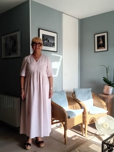 Cliente portant la Robe Agathe dans un salon. La robe longue rose pâle a une coupe fluide et un col en V.