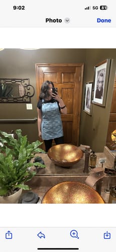 Reviewer taking a mirror selfie while wearing The Whitmore, a light-colored denim apron.