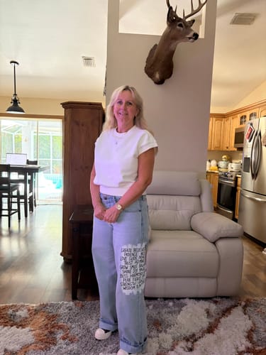 Reviewer standing in her living room, wearing the light-wash 'Positive Vibes' Painted Levi's Jeans with cuffed ankles.