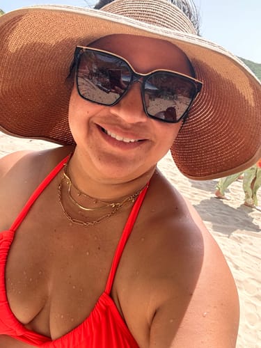Close-up of a customer smiling on a beach, wearing layered gold necklaces that look new after swimming.
