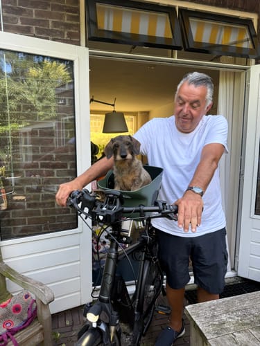 Customer's dachshund sitting in a green bike seat, enjoying a ride with the Comfort Seat Liner.