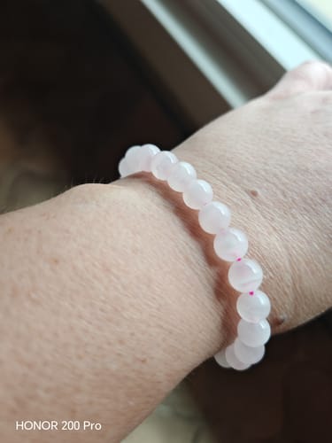 Cliente portant le bracelet en Manganocalcite au poignet, montrant les perles rose clair et l'élastique rose.