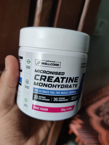 Reviewer holding a white tub of Wellcore Micronised Creatine Monohydrate in the Fruit Fusion flavor.