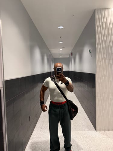 Customer taking a mirror selfie in a hallway, showing the fit of a white compression shirt.