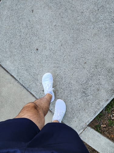 A customer's first-person view of their white Luck Ⅰ - Barefoot Shoes while standing on a sidewalk.