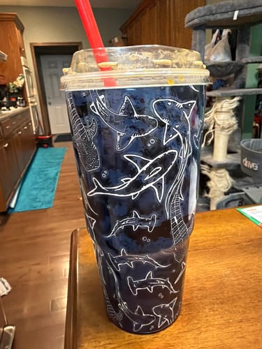Customer's To-Go Buddy in the Midnight Reef shark pattern, holding a cold drink with a straw on a wooden table.