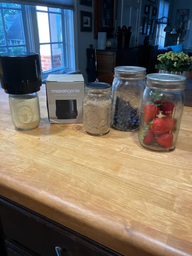 Reviewer's Mason Genie® vacuum sealer on a jar, with its box and other jars of fruit and dry goods on a counter.