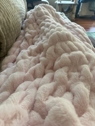 A close-up of the customer's pale pink Hugs Light Carnation Blanket, showing its soft, bumpy texture.