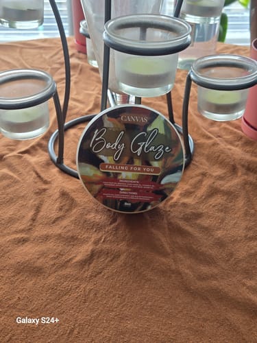 Customer's container of Body Glaze: Falling For You resting on a brown textured surface with a candle holder in the background.