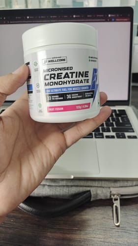 Customer's hand holding a white tub of Wellcore Micronised Creatine Monohydrate in Fruit Fusion flavor.