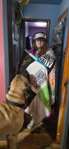 Customer holding up their custom Project Repat T-Shirt Quilt in a hallway as their dog looks on.