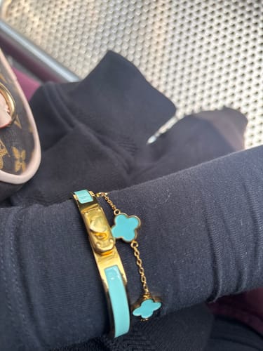 Kundin zeigt das goldene Türkis Clover Armband am Handgelenk, getragen im Set über einem schwarzen Ärmel.