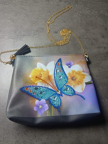 Rezensentin zeigt die fertige Diamond Painting Schultertasche mit einem Schmetterlingsmotiv aus blauen Glitzersteinen.