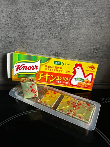 Reviewer's box of Ajinomoto Chicken Consomme Soup with the individual gold foil-wrapped cubes displayed on a cooktop.