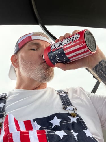 Customer drinking from a red 'We The People' Universal Buddy can cooler with a patriotic design.