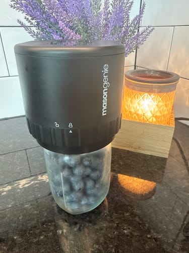 Customer using a black Mason Genie vacuum sealer on a jar of blueberries on a kitchen counter.
