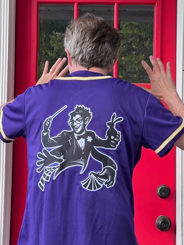 image 2 out of 2: Reviewer showing the back of the purple baseball jersey with a custom magician graphic.