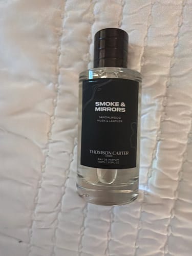 A customer's bottle of Smoke & Mirrors Eau de Parfum shown on a white, quilted surface.