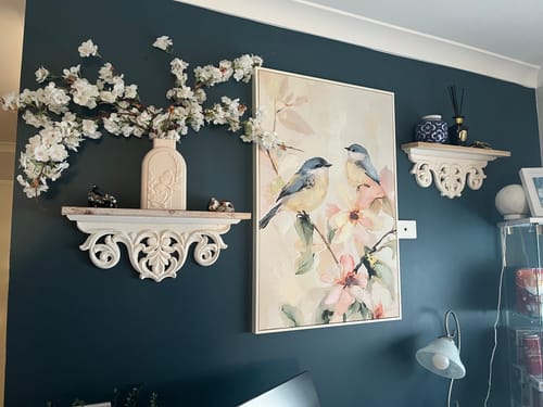 Customer's two white Natalie Mantel Shelves styled with decor and art on a dark blue wall.