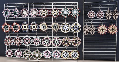 Customer photo showing numerous intricate, laser-cut earrings made with the AtomStack A70 Max, displayed on white racks.