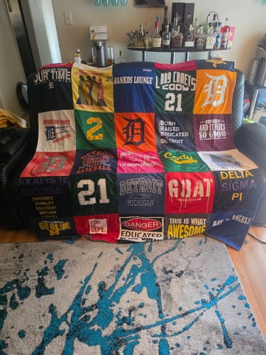 Customer's colorful Project Repat T-Shirt Quilt made from various graphic tees and jerseys, displayed on a living room sofa.
