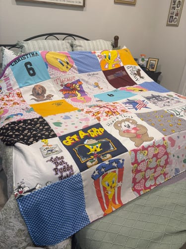 Customer's colorful Project Repat T-Shirt Quilt, made from shirts with cartoon graphics, shown at an angle on a bed.