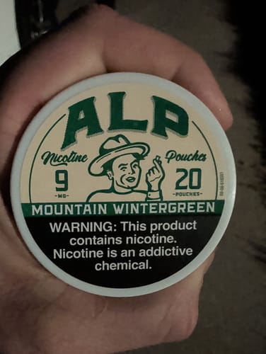 Customer holding a round can of ALP Mountain Wintergreen Nicotine Pouches.