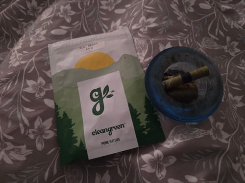 Customer's pouch of Roll Ready Ground flower resting on a floral blanket next to a blue ashtray.