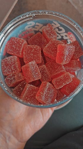 Ein Kunde hält einen offenen Behälter mit roten, gezuckerten THC Space Cubes in der Hand.