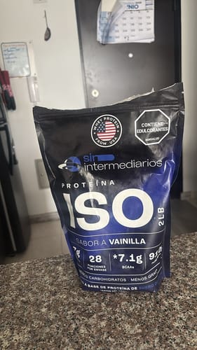 Reseñador muestra la bolsa negra y azul de Proteína ISO sabor vainilla, abierta sobre la encimera de una cocina.