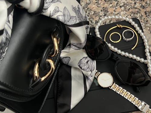 Customer's Ruby Petite Gold Silver watch shown in a stylish flat lay with a purse, sunglasses, and other jewelry.