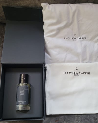 Customer's Lilium Blume Eau de Parfum unboxed, in its black packaging next to two white dust bags.