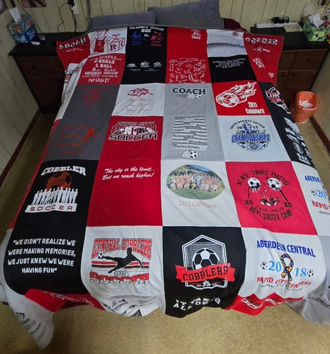 Customer's Project Repat T-Shirt Quilt with red, white, and gray soccer coaching shirts spread fully across a bed.