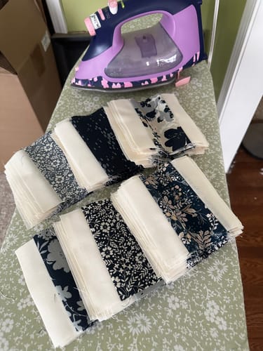 Reviewer's pre-cut navy and cream fabric blocks from the Dream Weaving Quilt Kit stacked on an ironing board.