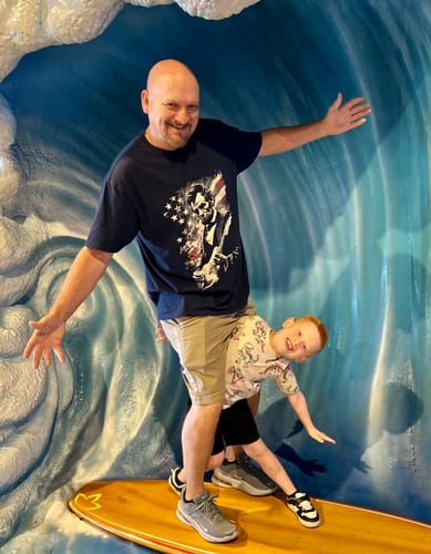 Customer wearing the Lincoln Flag T-Shirt while posing on a surfboard with a child.