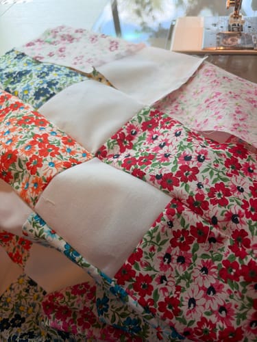 Close-up of a customer sewing the colorful floral and white pieces of the Brick Prairie Precut Quilt Kit.