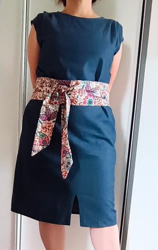 Cliente portant la ceinture Anita à monter soi-même, nouée sur une robe bleu foncé.