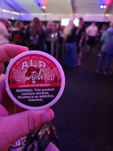 Customer's hand holding a white tin of Drifters Lemon Raspberry Nicotine Pouches at an event.